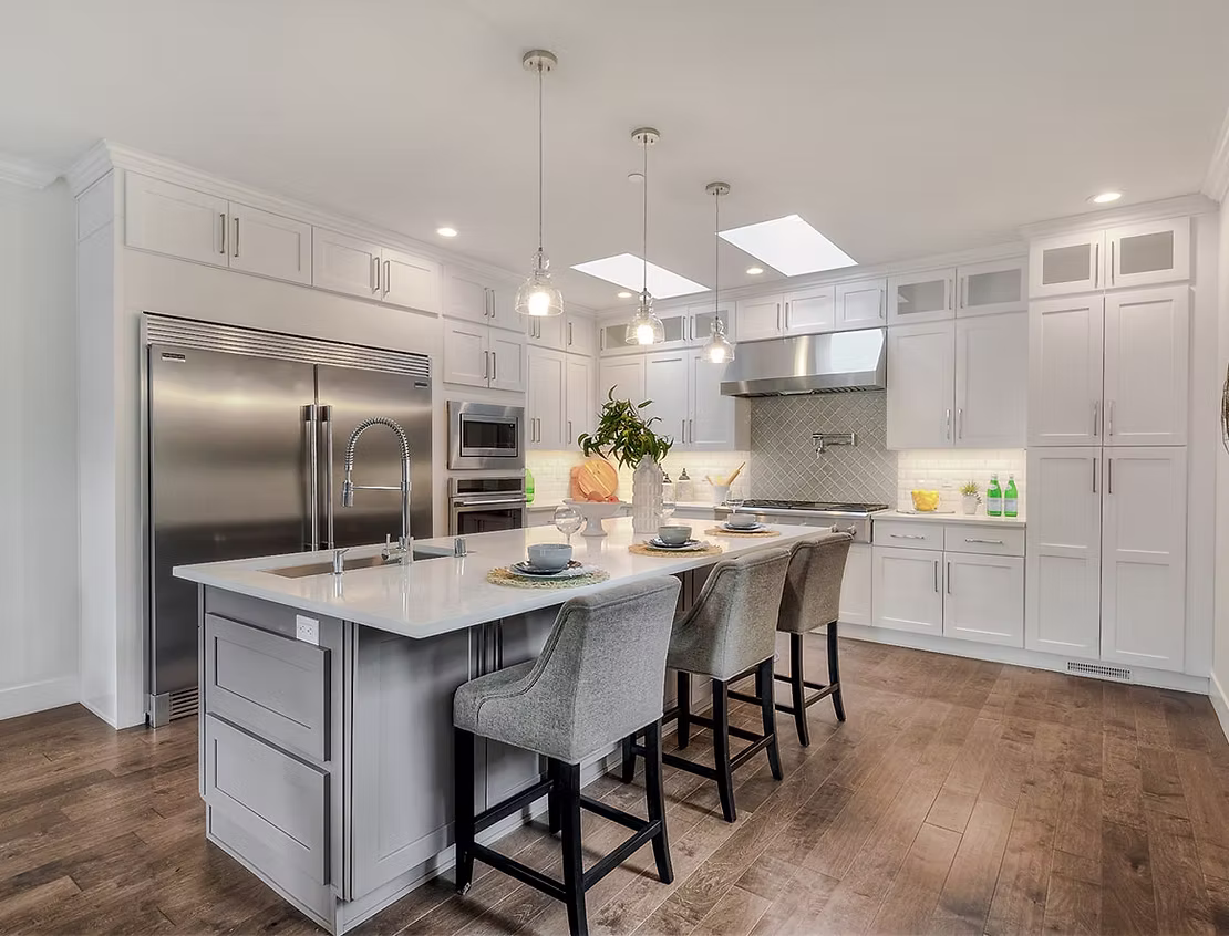 A luxury kitchen featuring a large gray island with seating, a white tile backsplash, and stainless steel appliances, demonstrating the quality of an ADHG build.