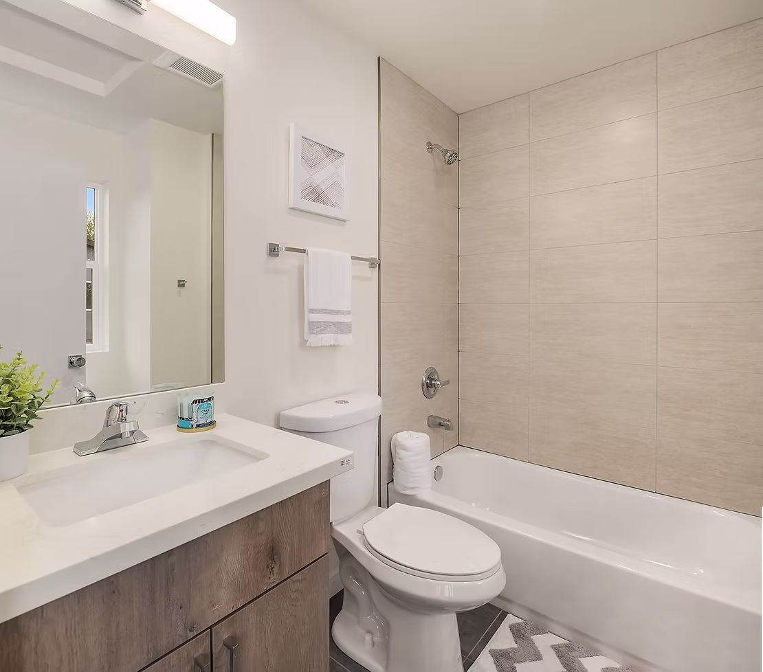A functional bathroom with a wood-grain vanity, a white countertop, and neutral-toned tiles, representing a standard high-quality finish in ADHG homes.