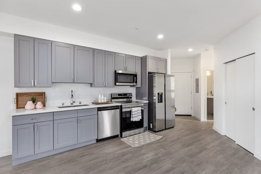 A contemporary apartment kitchen with gray cabinetry and stainless steel appliances, representing the premium interior finishes offered in the units.