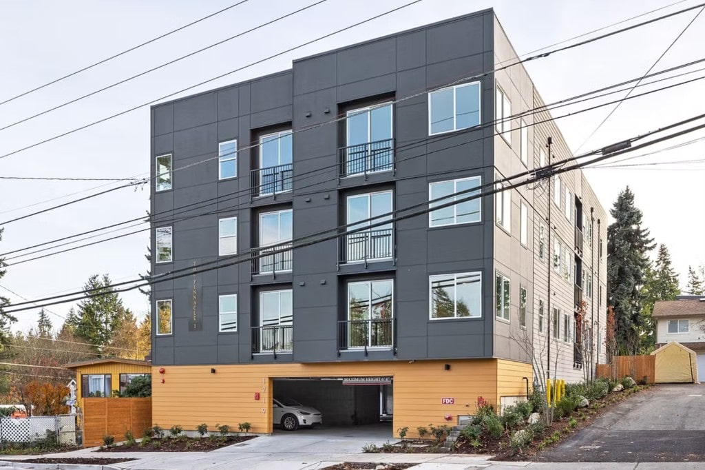 The exterior of 'The Pinnacle I,' a modern apartment building with dark gray paneling and covered parking, managed by DSM Sophia in WA.