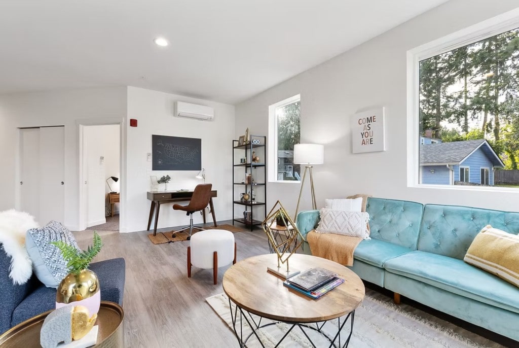 A bright, modern living room in an apartment unit, featuring a turquoise sofa, contemporary decor, and a dedicated home office area for prospective renters.