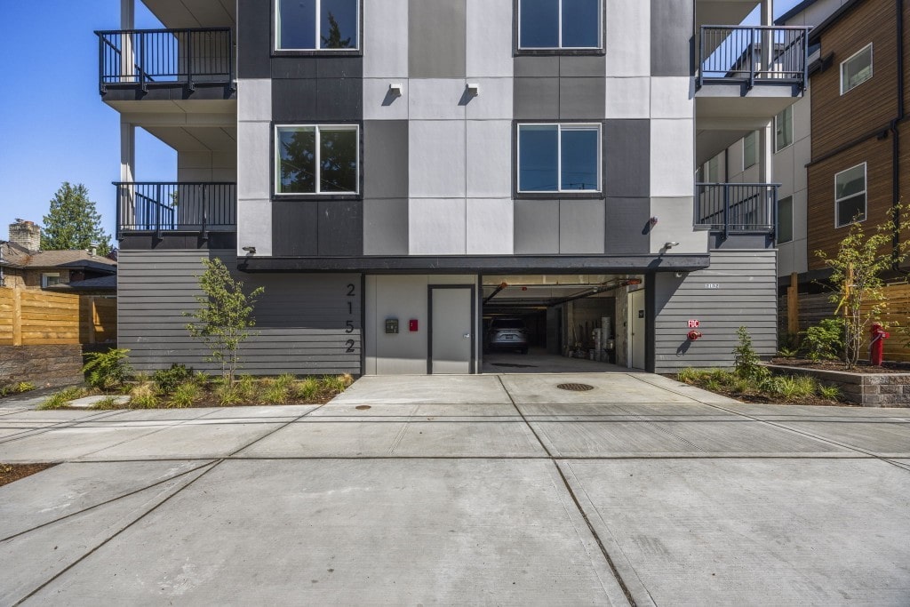 The front exterior of a modern multi-story apartment building with a checkered gray and white facade and a covered parking entrance.