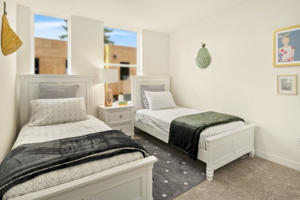 A brightly lit bedroom with two twin beds, white furniture, and playful wall decorations, showcasing a cozy and modern interior space.