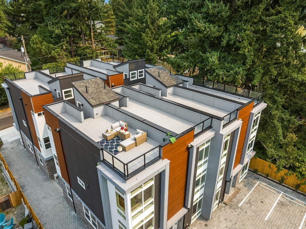 An aerial view of a modern townhouse development, showcasing the rooftop patio with outdoor furniture and the mixed-material exterior siding.