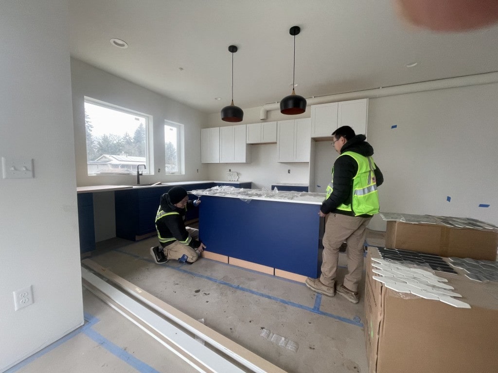 Construction workers installing a blue kitchen island and white upper cabinets, highlighting the attention to detail in the interior build phase.