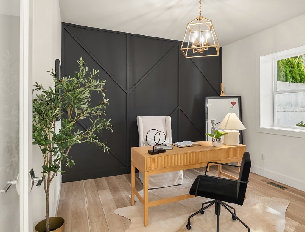 A stylish home office with a dramatic black accent wall featuring geometric paneling, a wooden desk, and modern light fixture.