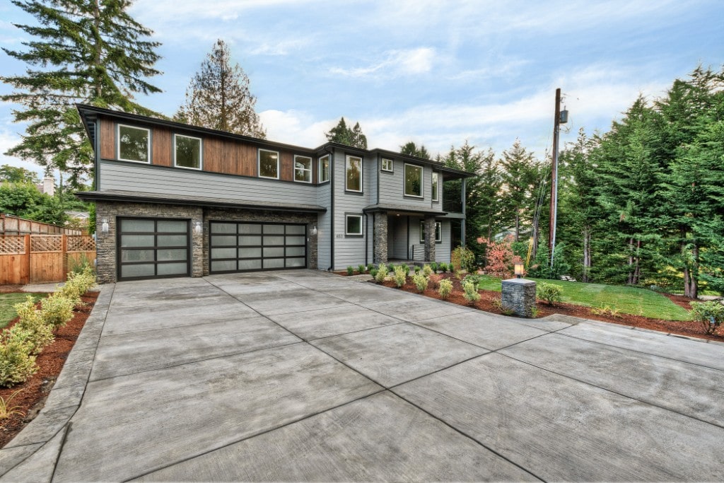 A striking modern single-family home with a large concrete driveway, two-car glass garage door, and stone accents, built by TP Home.