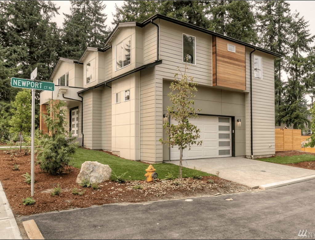 A modern two-story home with a clean beige and wood-panel facade on a corner lot, representing a finished residential property.
