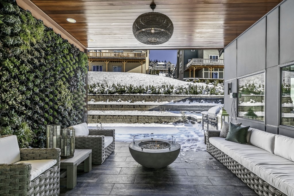 A luxurious covered outdoor patio in the snow, featuring a vertical moss wall and a concrete fire bowl, showcasing year-round outdoor amenities.