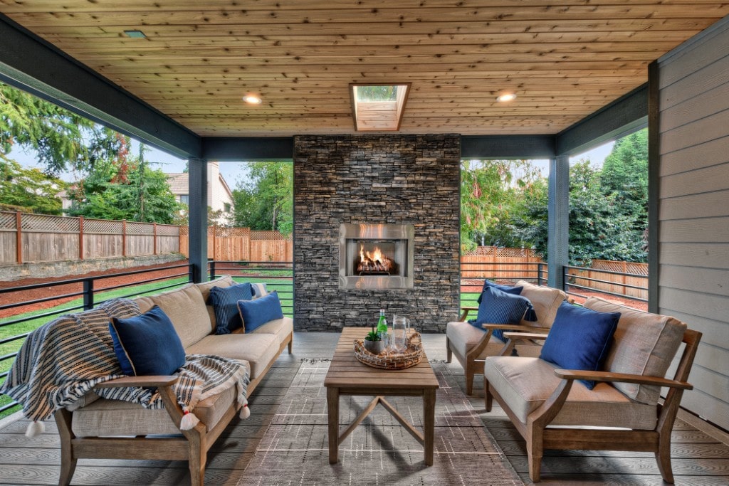 A luxury covered outdoor patio featuring a stacked stone fireplace and cozy seating, demonstrating premium outdoor living spaces in ADHG homes.
