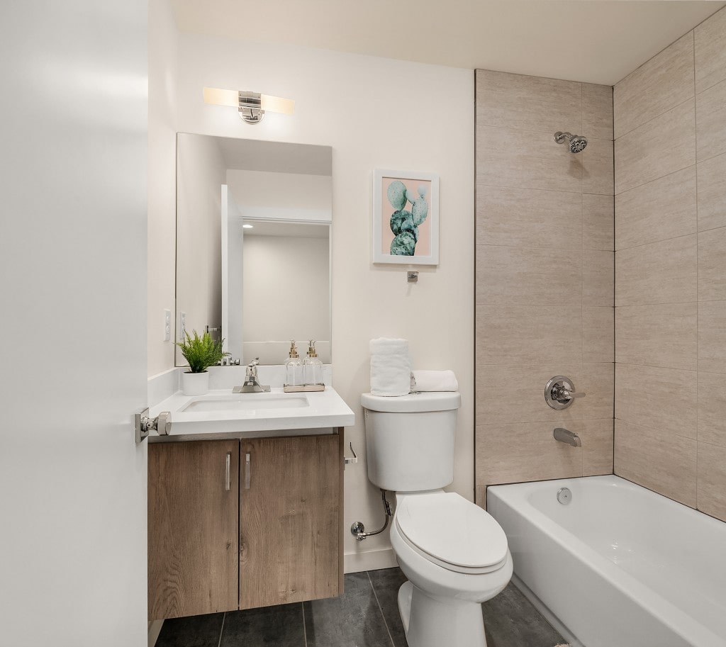 A contemporary bathroom with a light wood vanity, a white countertop, and a tiled shower-tub combo, representing a clean interior finish.
