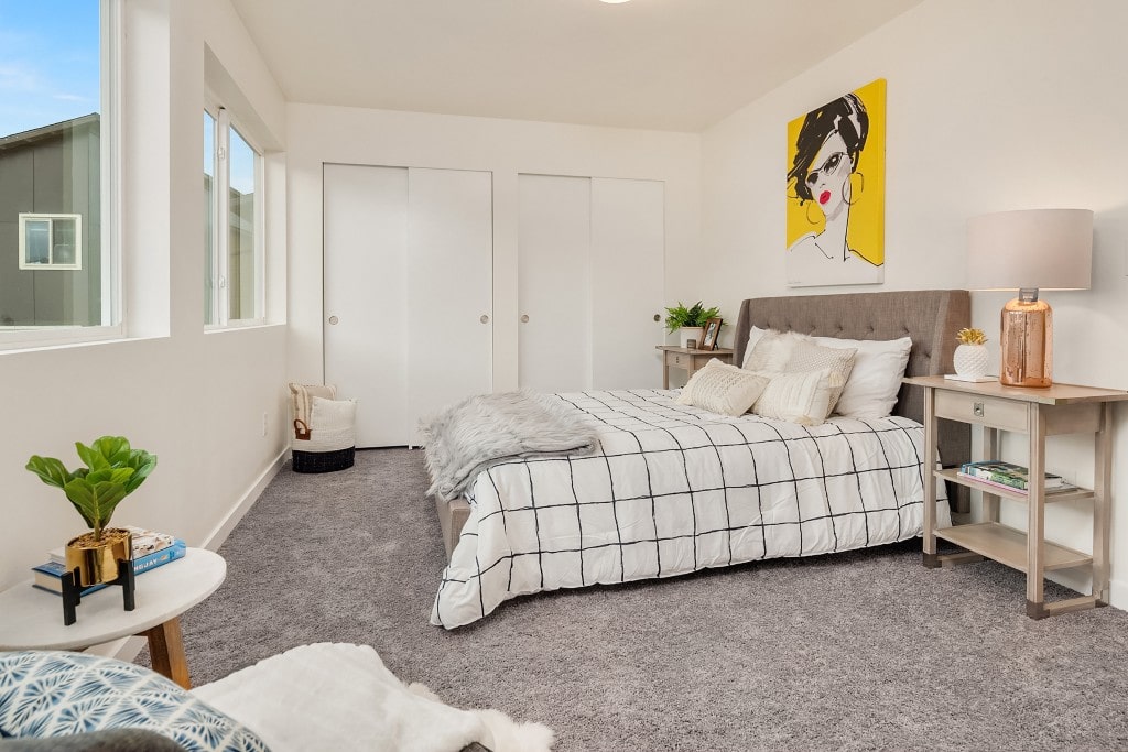 A bright and modern bedroom with a comfortable bed, large windows, and a colorful abstract painting, highlighting a clean and inviting design.