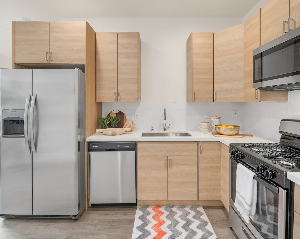 A modern kitchen with light wood-tone cabinetry, stainless steel appliances, and a tiled backsplash, showcasing the interior of a Monroe townhouse.