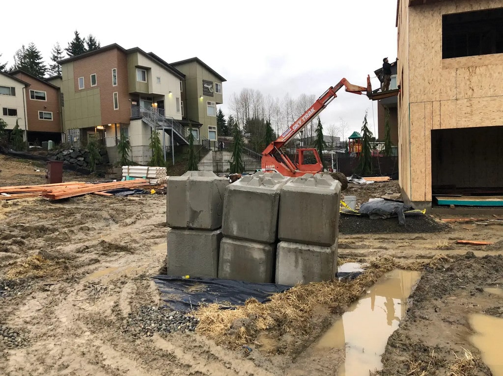 A construction site in Monroe with a muddy lot, concrete blocks, and a crane, representing the early stages of a townhouse development.