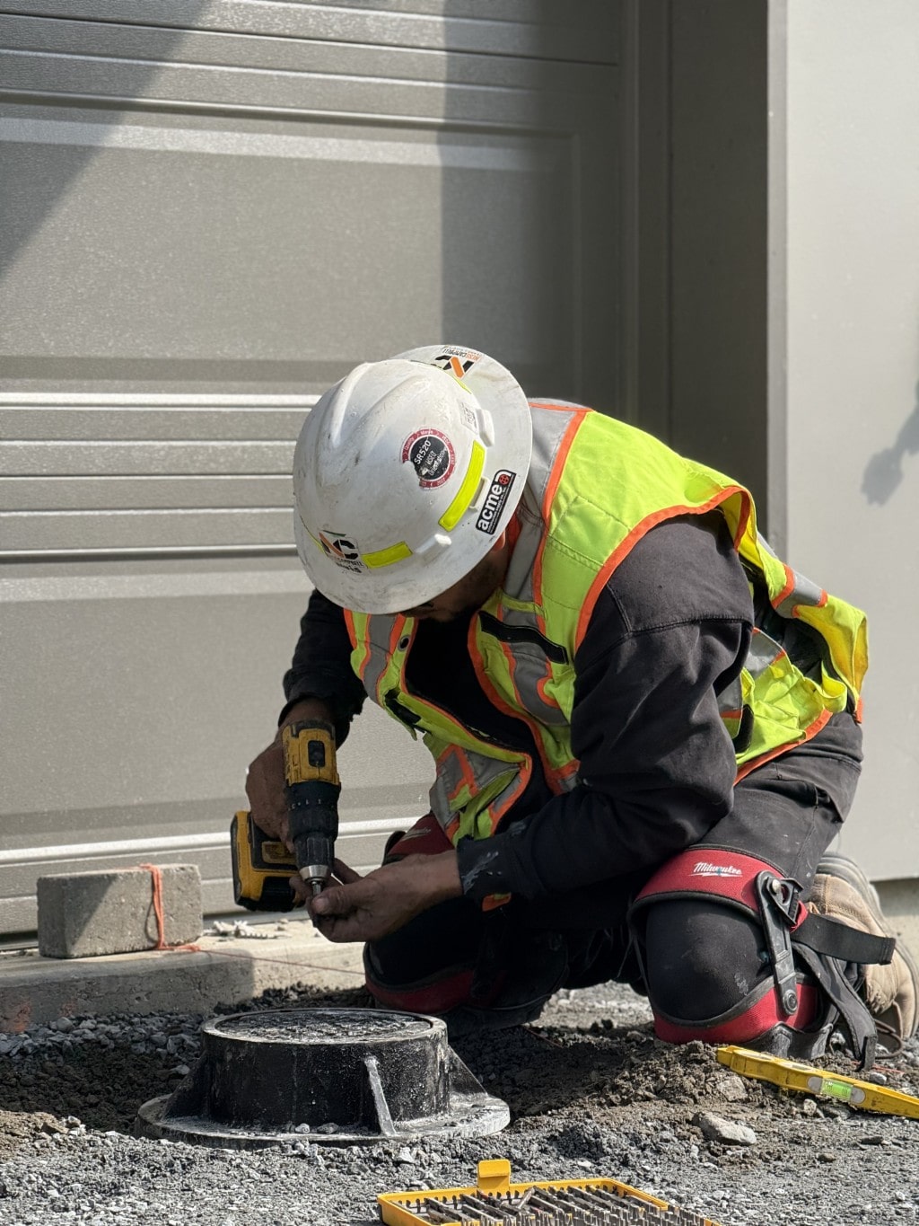 A worker installs a cover plate on a utility access point on the ground outside a garage, showing the finalization of site infrastructure.