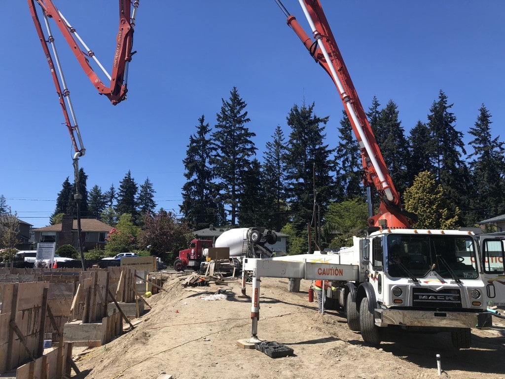 A concrete pump truck pours cement into foundation forms, showcasing the high-volume work required in the construction phase.