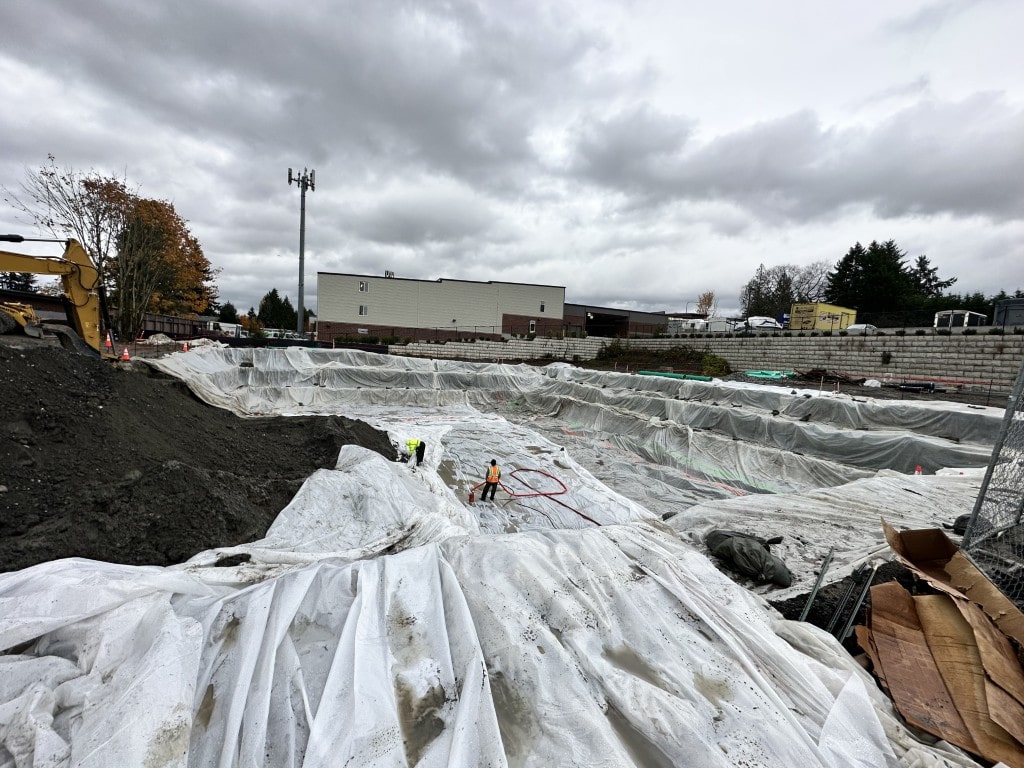 A large, leveled area on a construction site covered with white soil stabilization fabric, showcasing erosion control and grading work.