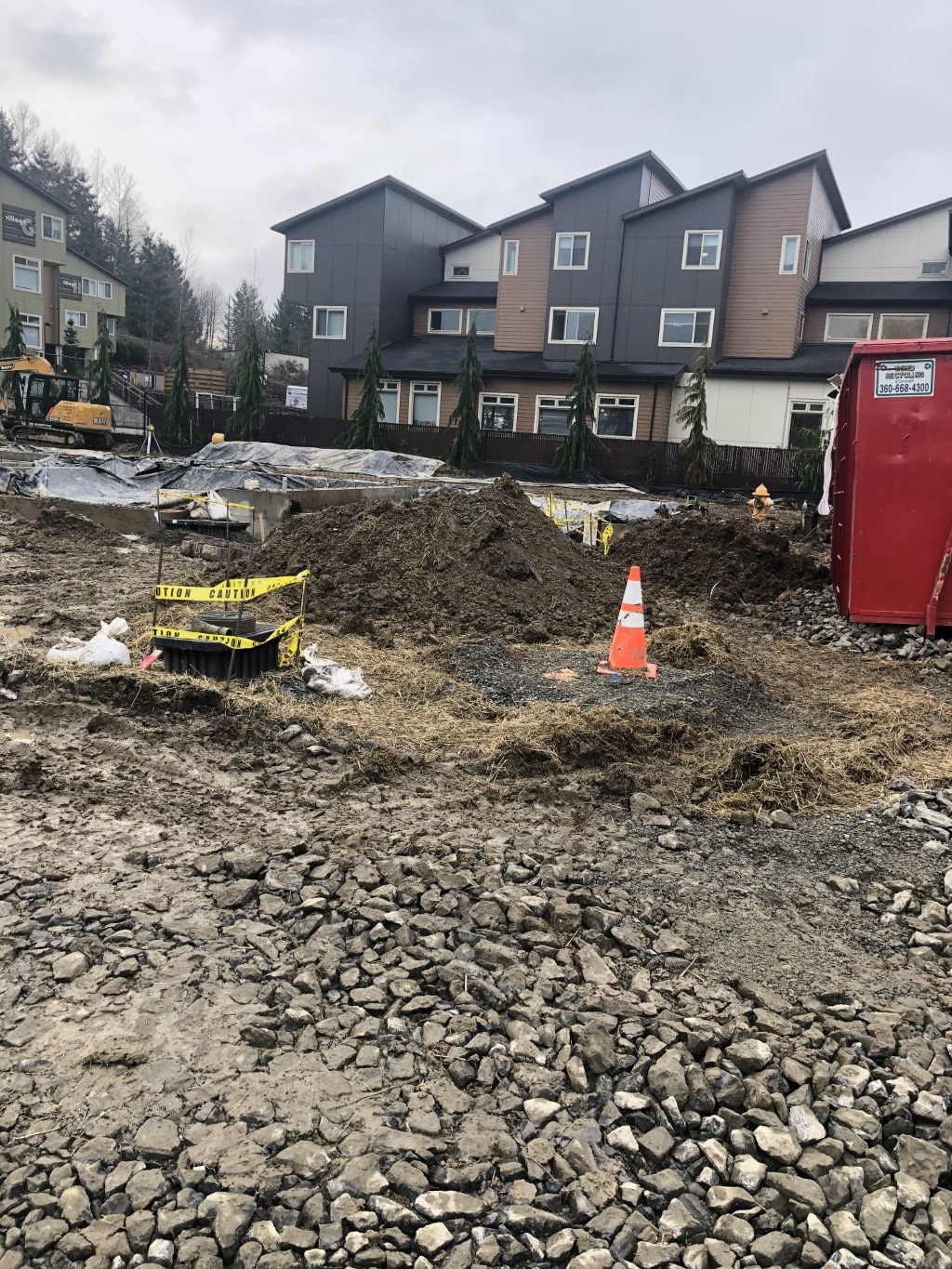 A muddy construction site with exposed rock and a dirt pile, highlighting the challenging site preparation and excavation conditions.