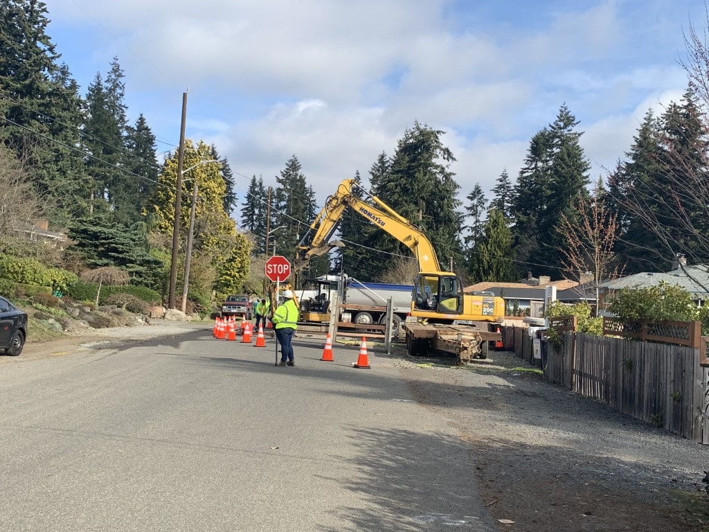 A worker directs traffic with a 'STOP' sign on a residential street, ensuring safety during heavy excavation work by ADHG's partners.