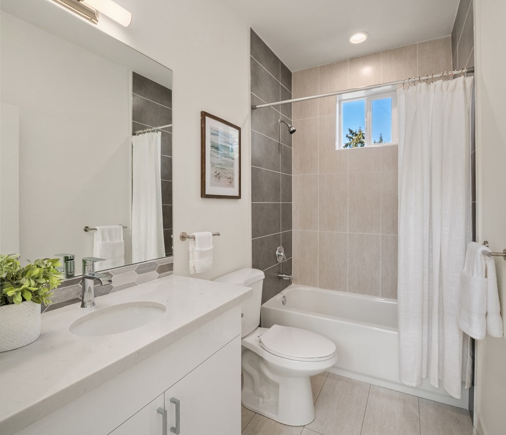 A contemporary bathroom with a light wood vanity, white countertops, and a tiled shower-tub combination, featuring a clean and elegant design.