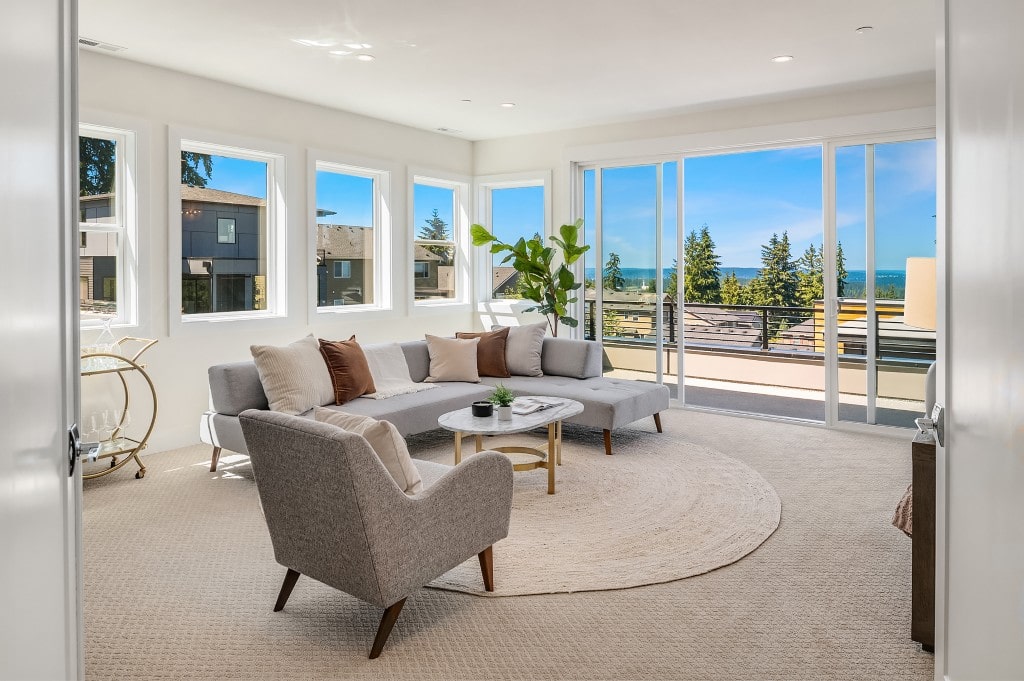 A modern living room with a panoramic view of the water and neighborhood, featuring a gray sectional sofa and a round rug, showcasing a premium ADHG build.