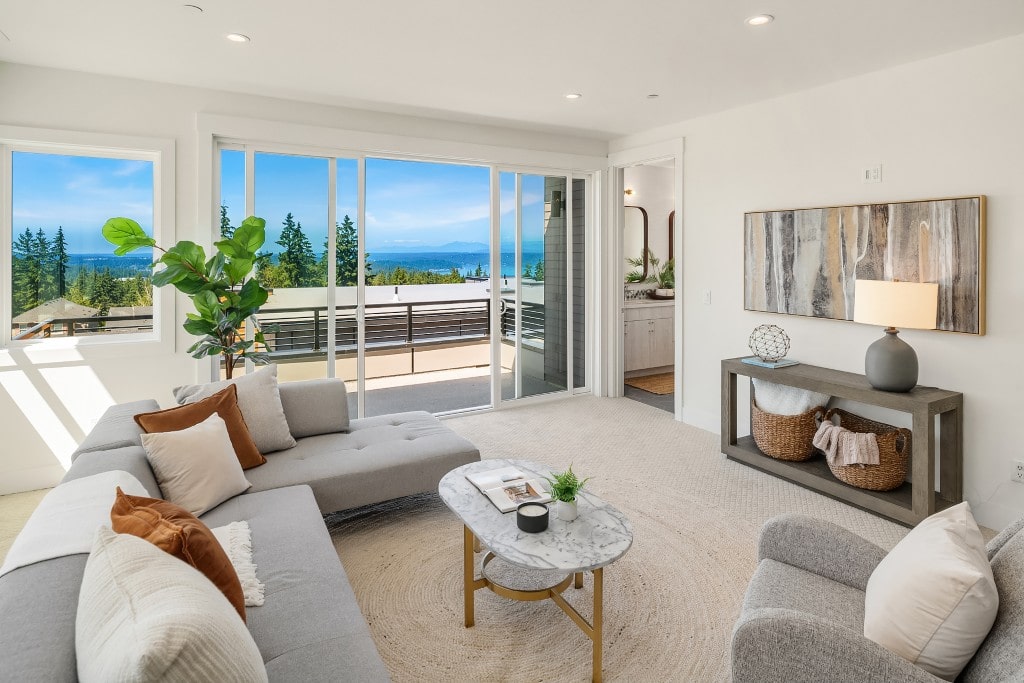 A bright living room with a comfortable sectional sofa and large sliding glass doors, offering a stunning water view from a Bellevue home.