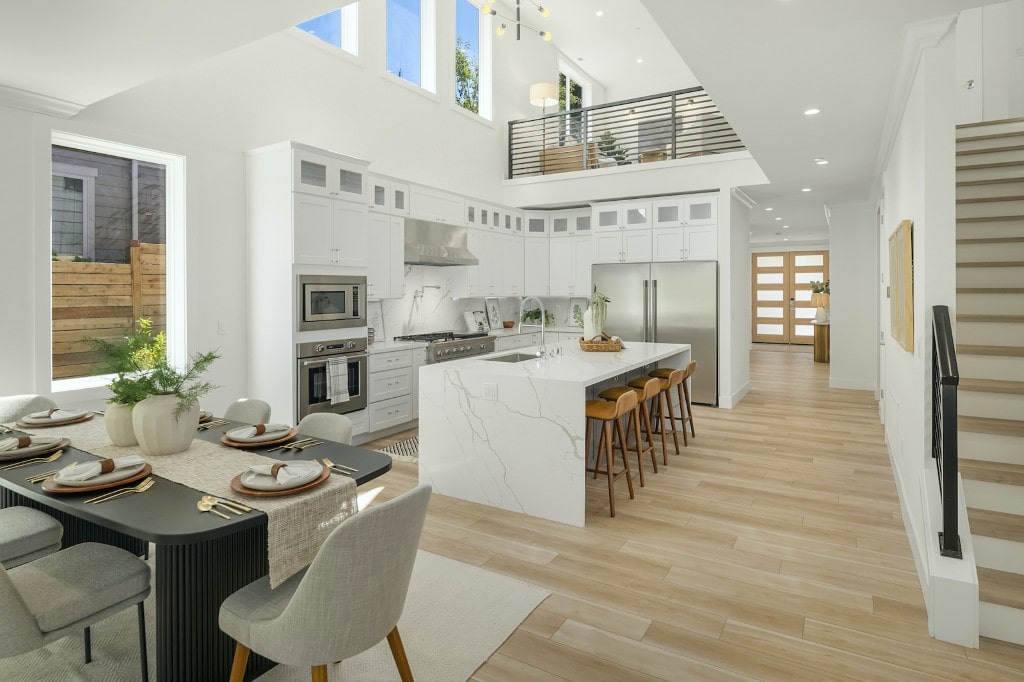 A bright, high-ceiling kitchen with white cabinets, a waterfall island, and a mezzanine-style loft, demonstrating a luxury design in a Bellevue home by ADHG.