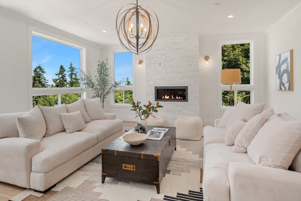 A bright living room with a modern fireplace, white stone accent wall, and large windows, showcasing a comfortable space designed by ADHG.