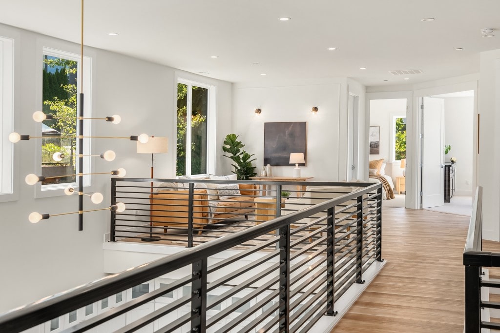 A view from a second-floor landing overlooking a bright living room, showcasing a modern interior with black metal railings and natural wood floors.